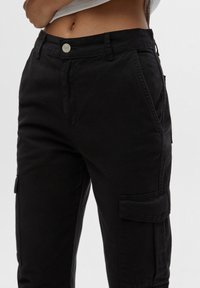 Pantalons cargo noirs en coton, avec poches latérales, fermeture à bouton et coupe décontractée. Texture lisse et détails de design décontracté.