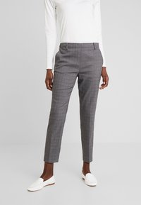 Grå rutiga byxor med skräddarsydd passform, med platt front och sidofickor, parat med vita loafers och en långärmad vit topp.