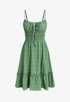 Groene mouwloze jurk met verstelbare bandjes, geplooide taille en gestructureerde stof. Heeft een gerimpelde zoom en een strikdetail aan de voorkant.