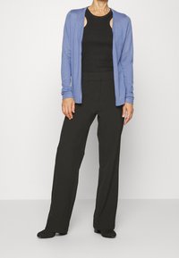 Cardigan bleu clair à manches longues porté sur un top noir sans manches, associé à un pantalon noir taille haute. Le tissu semble doux et lisse.