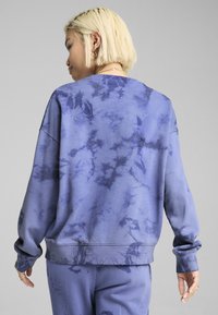 Felpa blu tie-dye con vestibilità comoda, collo rotondo e maniche lunghe. Tessuto morbido con una combinazione di tonalità di blu più chiare e più scure.