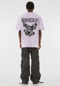 Lilla oversized t-shirt med sort sommerfugl grafik på ryggen og teksten "MYGONZALEZ" ovenfor, parret med sorte cargo bukser.