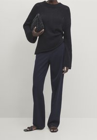 Mustat neulotut neuleet pitkillä hihoilla, yhdistettyinä tummansinisiin leveälahkeisiin housuihin. Kädessä pidetään teksturoitua mustaa clutch-laukkua. Litteät sandaalit viimeistelevät asun.