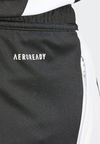 Svart athletic shorts med hvite detaljer, med en glidelåslomme og «AEROREADY»-logoen på venstre lår, glatt tekstur.