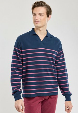 Polo shirt à manches longues marine avec des rayures horizontales roses, présentant une texture douce et une coupe décontractée, avec un col en V.