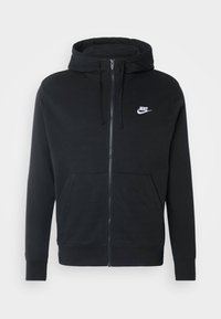 Svart zip-up hoodie gjord av en bomullsblandning, med en känguruficka, snörad huva och liten vit Nike-logotyp på bröstet.