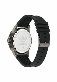 Melna gumijas siksna pulkstenis ar nerūsējošā tērauda korpusu, atstarojošu sudraba aizmuguri ar Adidas logo, teksturētu siksnu un izturīgu sprādzi.