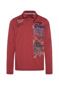 Rotes Langarm-Polohemd mit Kragen, das auf der linken Seite grafische Drucke in Blau, Schwarz und Weiß sowie einen strukturierten Stoff aufweist.