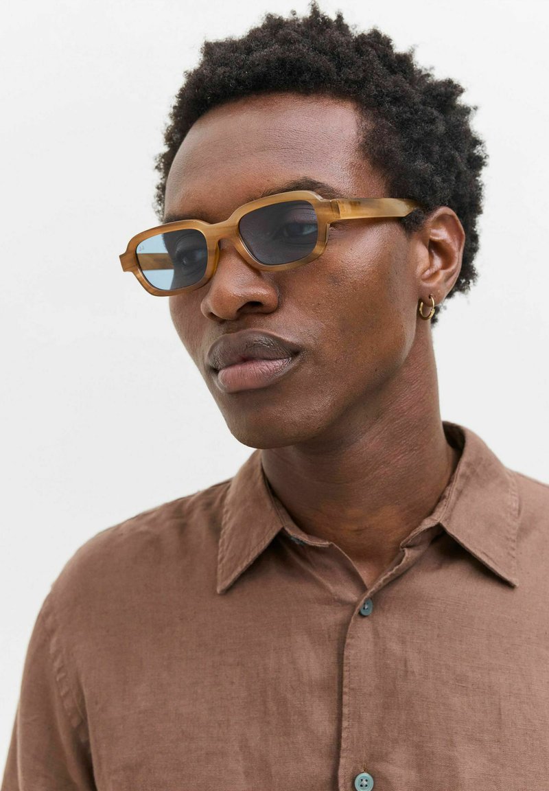 Brown-tinted sunglasses with a rectangular shape, made of a transparent material, featuring blue-tinted lenses and a subtle textured finish.
