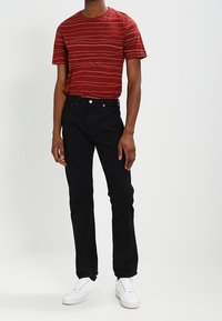 Punainen raidallinen lyhythihainen T-paita pyöreällä pääntiellä, yhdistettynä mustiin suoriin farkkuihin ja valkoisiin tennareihin. Yksinkertainen, rento ilme.