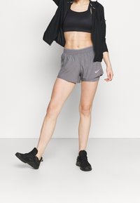 Gray athletic shorts with an elastic waistband, paired with a black cropped top and black sneakers. The shorts feature a subtle Nike logo.