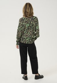 Loose-fitting long-sleeve top in green and black leopard print, paired with black tapered trousers and chunky black shoes.