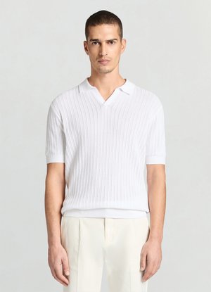 Polo en tricot côtelé blanc avec manches courtes et col en V. Texture lisse avec un col contrastant. Porté avec un pantalon de couleur claire.