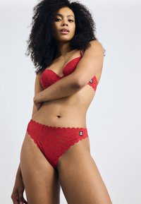 Red lace bra and matching thong, featuring scalloped edges, floral pattern, and tag on the side. Soft texture with underwire support.