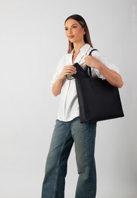 Zwarte leren tote bag met twee handvatten, met een gestructureerde vorm en een textuurovervlak. Een kleine zwarte portemonnee bevindt zich erin.