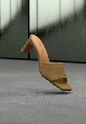 Μπεζ τακούνι mule με λεία, ματ υφή, σχέδιο ανοιχτής μύτης και καμπυλωτό λουράκι πάνω από το πόδι. Το τακούνι είναι γωνιώδες και μεσαίου ύψους.