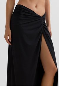 Črna ovijajoča krila iz mehke tkanine, s prepletenim dizajnom v predelu pasu in visokim razporkom na eni strani.