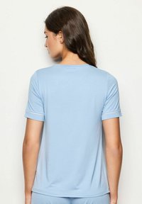 Lichtblauwe t-shirt met korte mouwen, ronde halslijn en omgeslagen mouwuiteinden. Gladde stof met een subtiele textuur en geen zichtbare patronen.