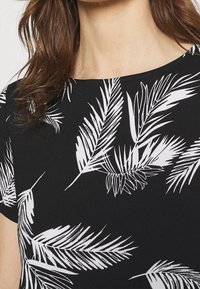 Černý top s bílými vzory palmových listů, krátké rukávy a kulatý výstřih. Hladká textura s volným střihem.