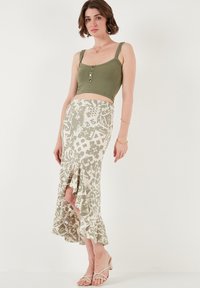 Zaļš ribots cropped tops ar pogām kopā ar krēmīgu svārku, kuram ir zaļš ziedu raksts un volāns apakšā. Nēsā ar vieglām sandālēm.