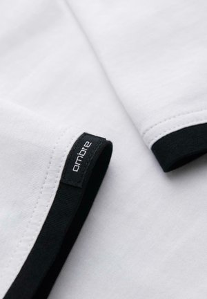 Hvidt stof med sort kant og "ombre" mærke syet nær kanten på et foldet plagg.