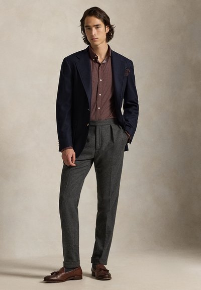 Blazer azul marinho, camisa de padrão borgonha, calças de lã cinza, mocassins de couro castanho. O blazer tem botões dourados; a camisa apresenta pequenos pontos.