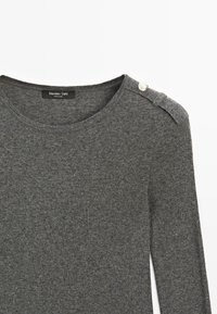 Top en maille gris foncé à manches longues avec un col rond et un détail de bouton argenté sur l'épauulière gauche.