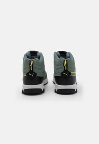 Green textile sneakers with black and white accents. Features a padded collar, textured design, and reflective yellow stripe. PUMA logo displayed.
