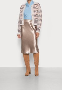 Knitted cardigan in light beige with patterned design, blue top, shiny bronze skirt, and tan over-the-knee boots with a chunky heel.