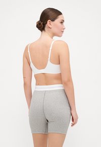 Sutiã branco com alças ajustáveis, apresentando um design de costas baixas. Combinado com calções canelados cinzentos, realçados por uma cinta branca em contraste.