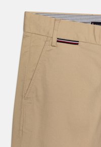 Chinos in cotone beige con una trama liscia, dotati di una tasca frontale e di una cinta a strisce in blu navy, rosso e bianco.