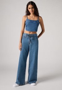 Top cropped de denim com alças finas, combinado com calças de denim de perna larga, ambos em azul médio, apresentando uma textura suave e detalhes mínimos.