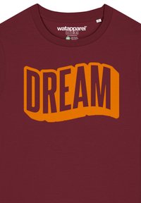 T-shirt en coton bordeaux avec un grand design graphique "DREAM" en jaune-orange dans une police stylisée et texturée, centré sur la poitrine.