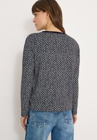 Bluzka z długim rękawem w kolorze granatowym z geometrycznym białym wzorem, z okrągłym dekoltem i luźnym krojem, zestawiona z jasnoniebieskimi dżinsami.