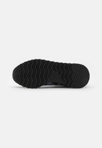 Sorte gummisåle til sneakers med en bølgete tekstur, som har en fremtredende triangulær logo i midten og glatte kanter for bedre grep.