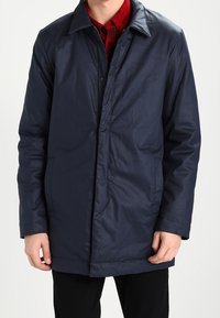 Navyblauer Nylonmantel mit klassischem Kragen, Knopfverschluss und zwei Seitentaschen; glatte Textur, knieumspielendes Design, minimalistisch im Stil.