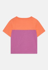 Camiseta de manga corta con una sección superior naranja y una sección inferior púrpura. Hecha de algodón suave con un sencillo cuello redondo.