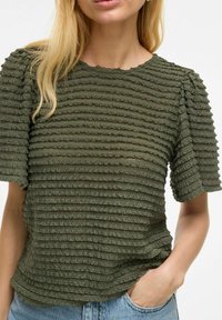 Top texturizado en verde oliva con un patrón de rayas horizontales, mangas cortas abullonadas y cuello redondo, confeccionado en una tela suave. Corte casual.