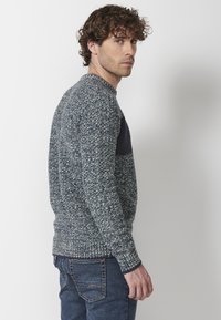 Suéter de punto en azul y gris, con un cuerpo texturizado y un panel suave en marino en la parte superior. Puños y dobladillo acanalados. Llevado con jeans de mezclilla.