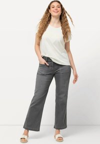 Jeans gris de pierna ancha con bolsillos frontales, combinados con una camiseta blanca de corte holgado con texto en cursiva amarilla. Llevados con sandalias de color claro.