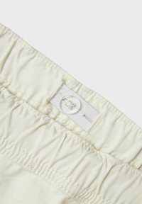 Crèmegekleurde stof met een gladde textuur, voorzien van een elastische tailleband en een witte knoopsluiting. Gathered ontwerp voor extra rek.