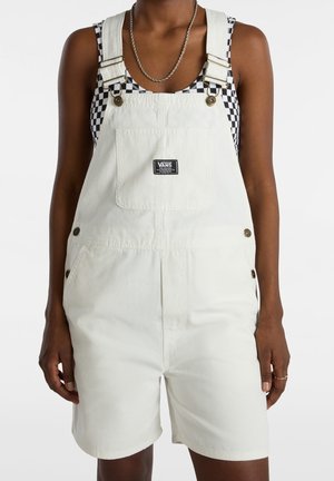Kvinde iført hvide korte overalls fra Vans og en sort-hvid ternet ærmeløs top med sølvkæde halskæde.