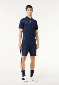 Camisa polo navy de manga corta y cuello, combinada con pantalones cortos a juego. Presenta una tapeta de botones blanca y un logo verde en los pantalones cortos.