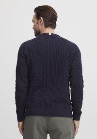 Pull marin avec un design en tricot à torsades texturées, des poignets et un ourlet côtelés. Une petite touche de couleur au niveau du col ajoute un détail.