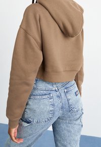 Avklippt brun hoodie med huva, kombinerad med ljusblå, högmidjade jeans med plåtfickor och en blekt struktur.