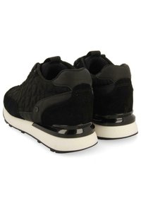 Zapatos deportivos negros con un diseño acolchado en la parte superior, detalles de ante y una entresuela blanca. Superficies suaves y texturizadas en los lados y la parte trasera.