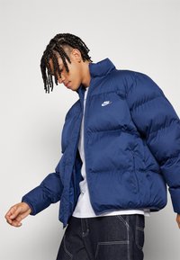 Μπλε φούτερ μπουφάν με φερμουάρ στο μπροστινό μέρος, ψηλό γιακά και λογότυπο Nike στο στήθος. Διαθέτει ραφές με πλέξη και ελαστικούς καρπούς.