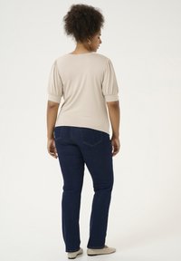 Beige topp med puffärmar, i kombination med mörkblå jeans. Slät tyg och skräddarsydd design. En enkel, skräddad look utan prydnader.
