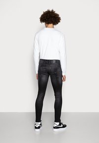 Vaqueros negros ajustados con una textura desgastada, bolsillos traseros y una etiqueta minimalista. Combinados con una camiseta blanca de manga larga y zapatillas negras.