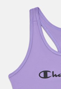 Violeta sporta krūšturis ar sacensību aizmuguri un daļēju melno Champion logotipu priekšpusē, attēlots uz baltas fona.